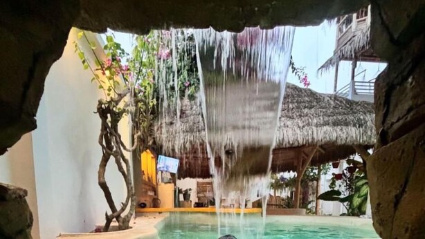 Ein Pool mit klarem Wasser, eine Person in der Mitte und ein Wasserfall.