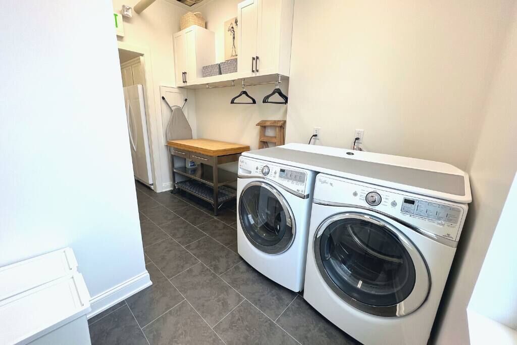 A laundry room with two front-loading washing machines, a wooden bench, and a small table.