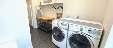 A laundry room with two front-loading washing machines, a wooden bench, and a small table.