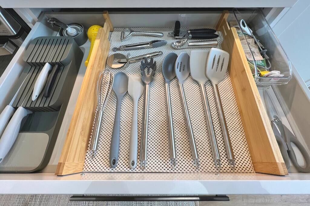 A kitchen drawer with various utensils neatly organized, including spatulas, tongs, and a grater.