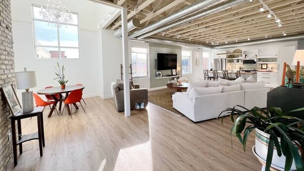 A spacious living area with a modern design, featuring a white sofa, a dining table with red chairs, and a kitchen area in the background. - The Quarters | Suite 1 (Grafton)