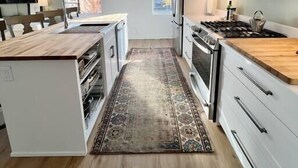 A modern kitchen with white cabinetry, a wooden island, stainless steel appliances, and a large window providing natural light. - The Quarters | Suite 1 (Grafton)