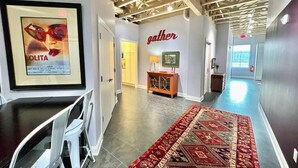 A hallway with a red patterned rug, a framed poster on the wall, and a 'gather' sign. - The Quarters | Suite 3 (Grafton)