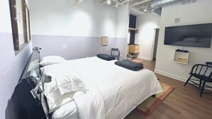 A hotel room with a large bed, a TV mounted on the wall, and a chair. - The Quarters | Suite 3 (Grafton)