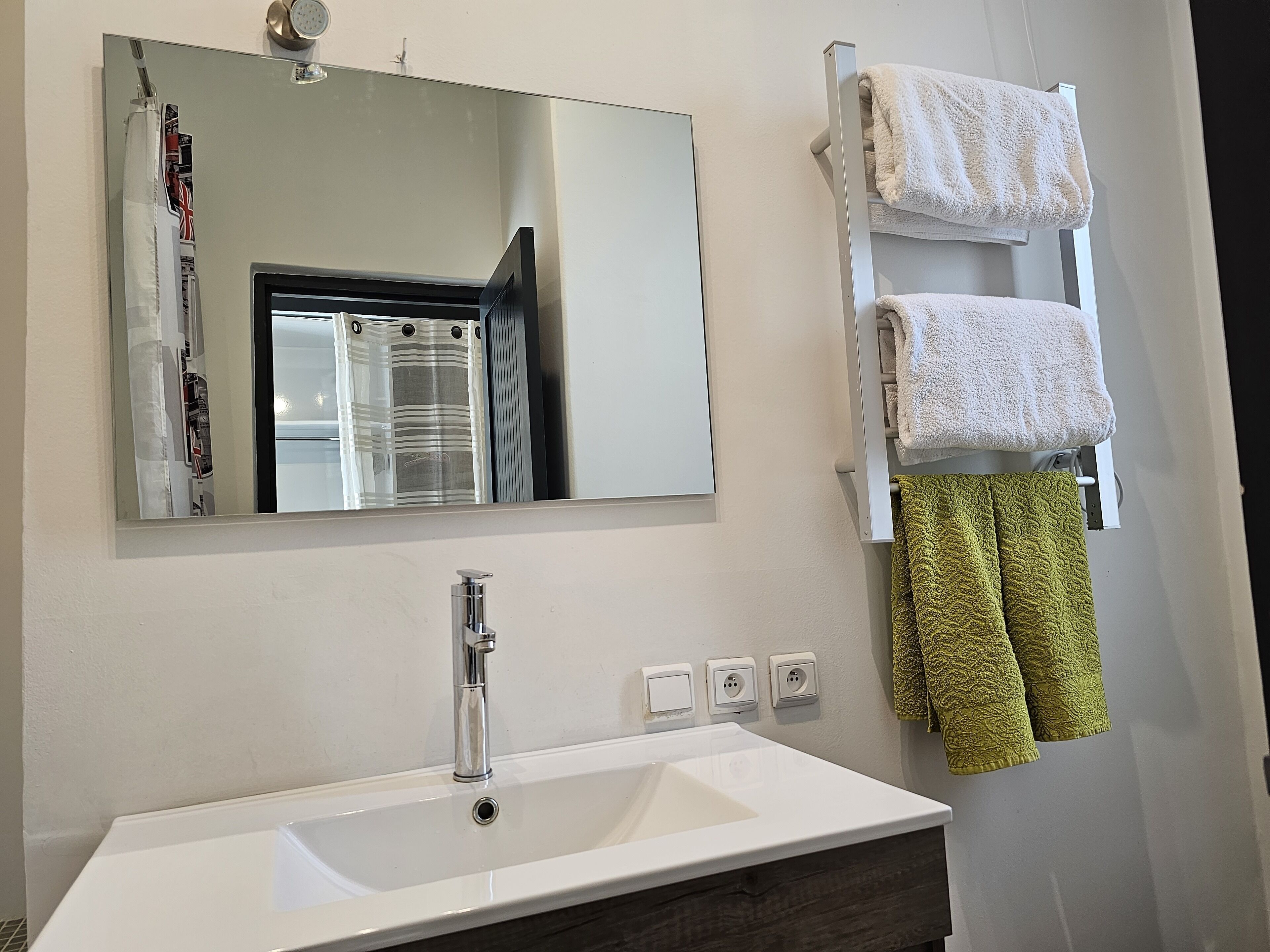 Un baño con un lavamanos blanco, un espejo y un toallero con toallas blancas y verdes.