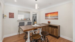 Un comedor con una mesa de madera, taburetes de bar y una cocina al fondo.