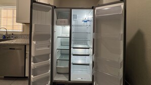Una cocina en esquina con refrigerador empotrado, un lavamanos y una ventana con persianas.