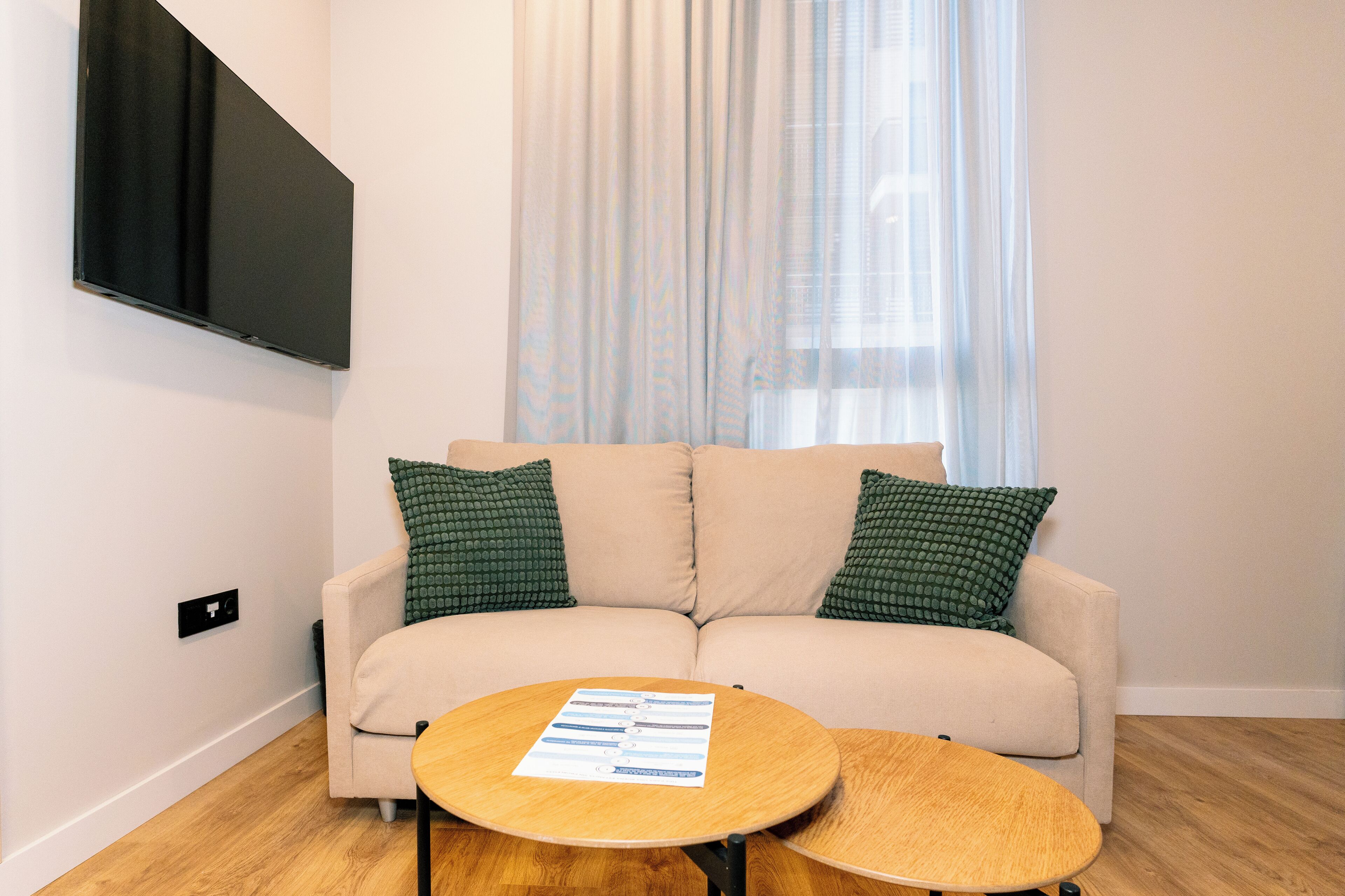 A living room with a beige sofa, two green patterned pillows, and a wooden coffee table with documents.