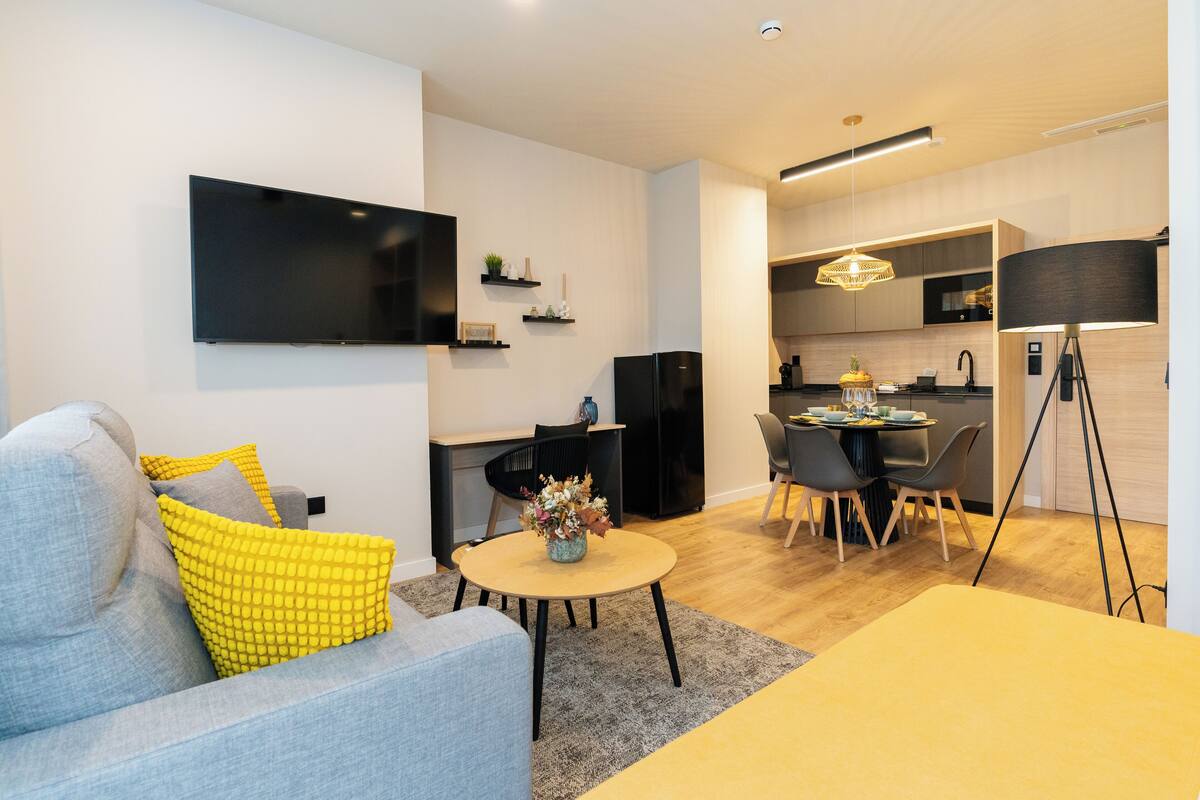 A modern living room with a sofa, a dining table, and a kitchen area in the background.