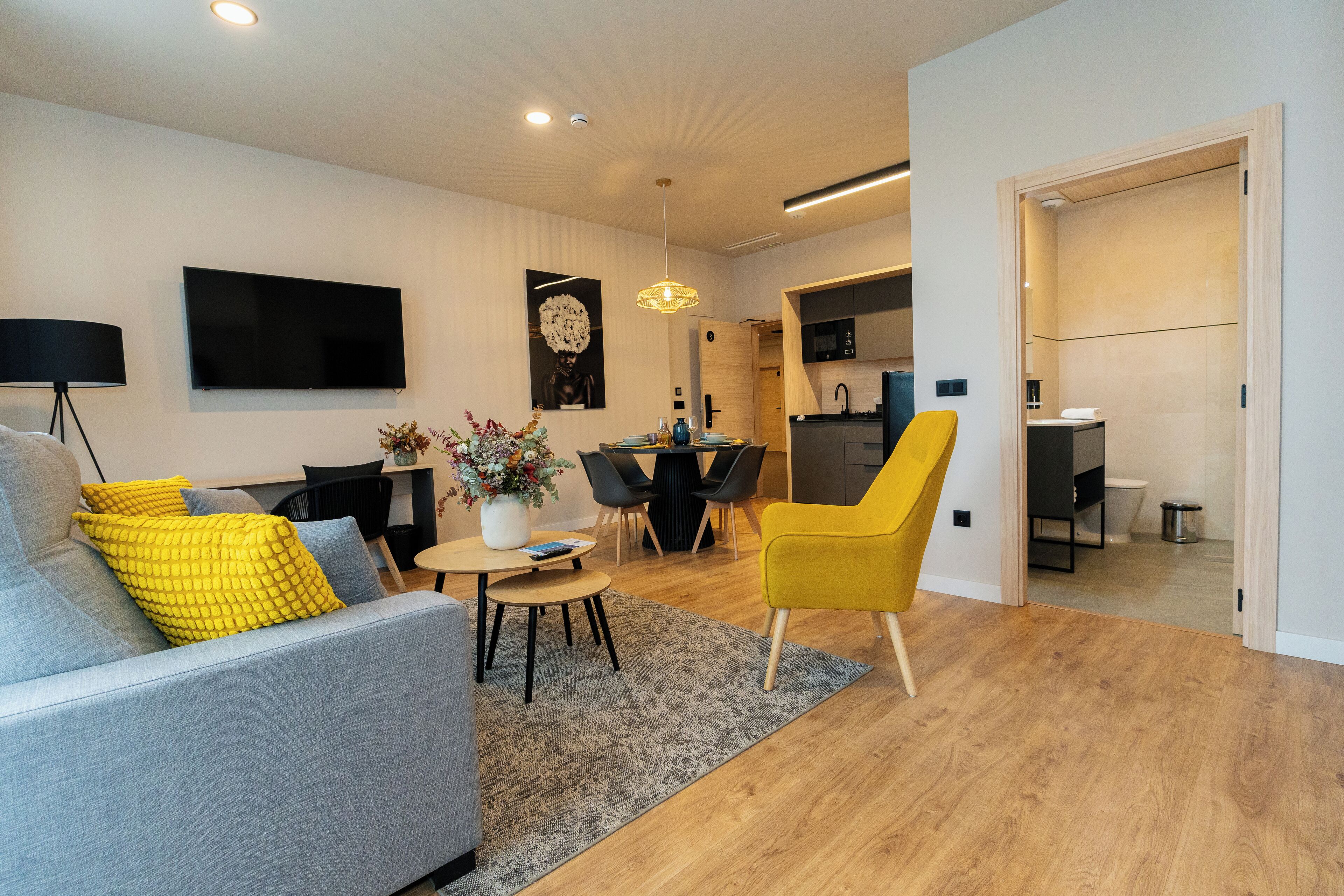 En moderne stue med en sofa, en gul lænestol, et spisebord og et køkken i baggrunden.