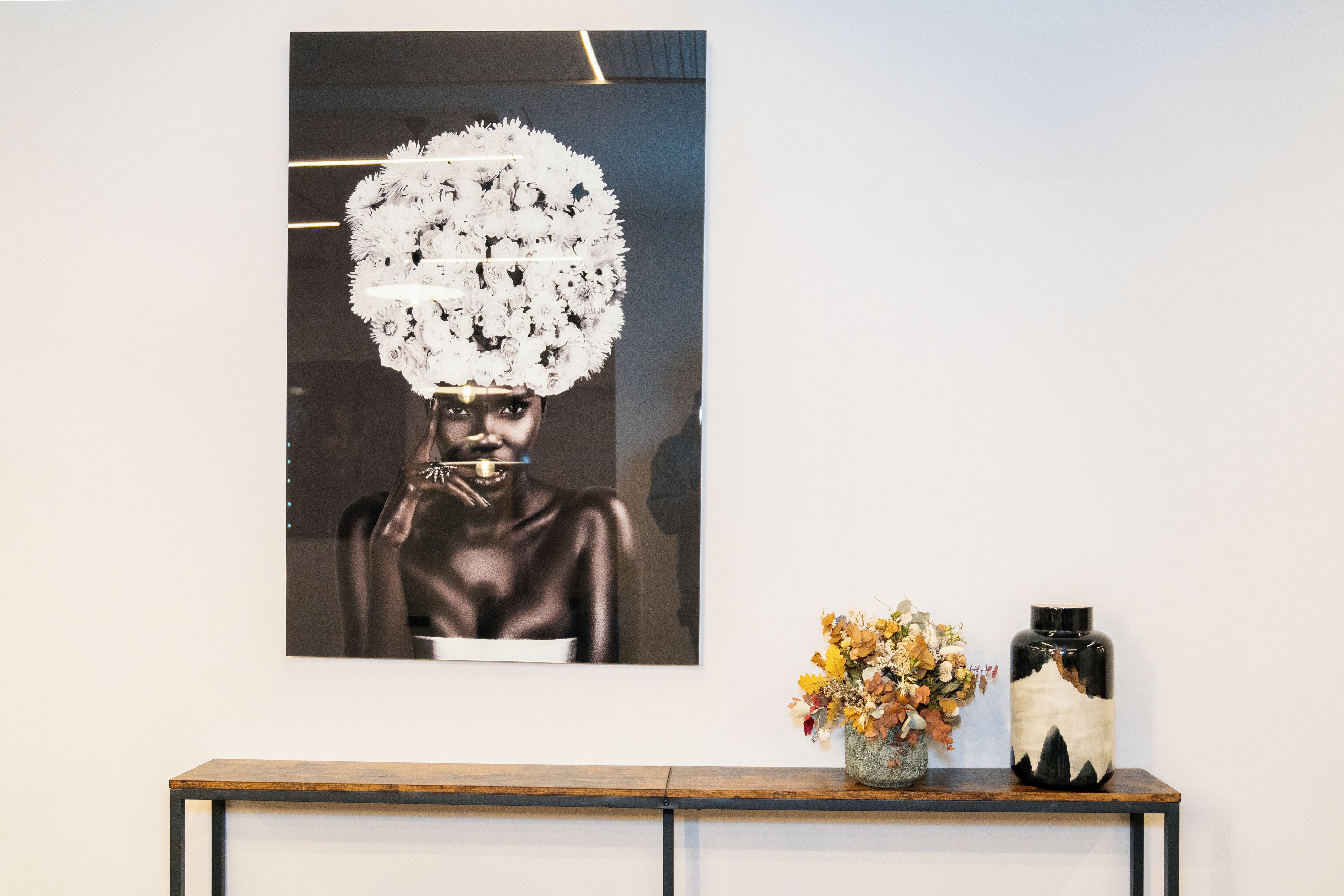 A framed artwork on a wall, a wooden console table with a vase of dried flowers, and a ceramic vase with a black and white design.
