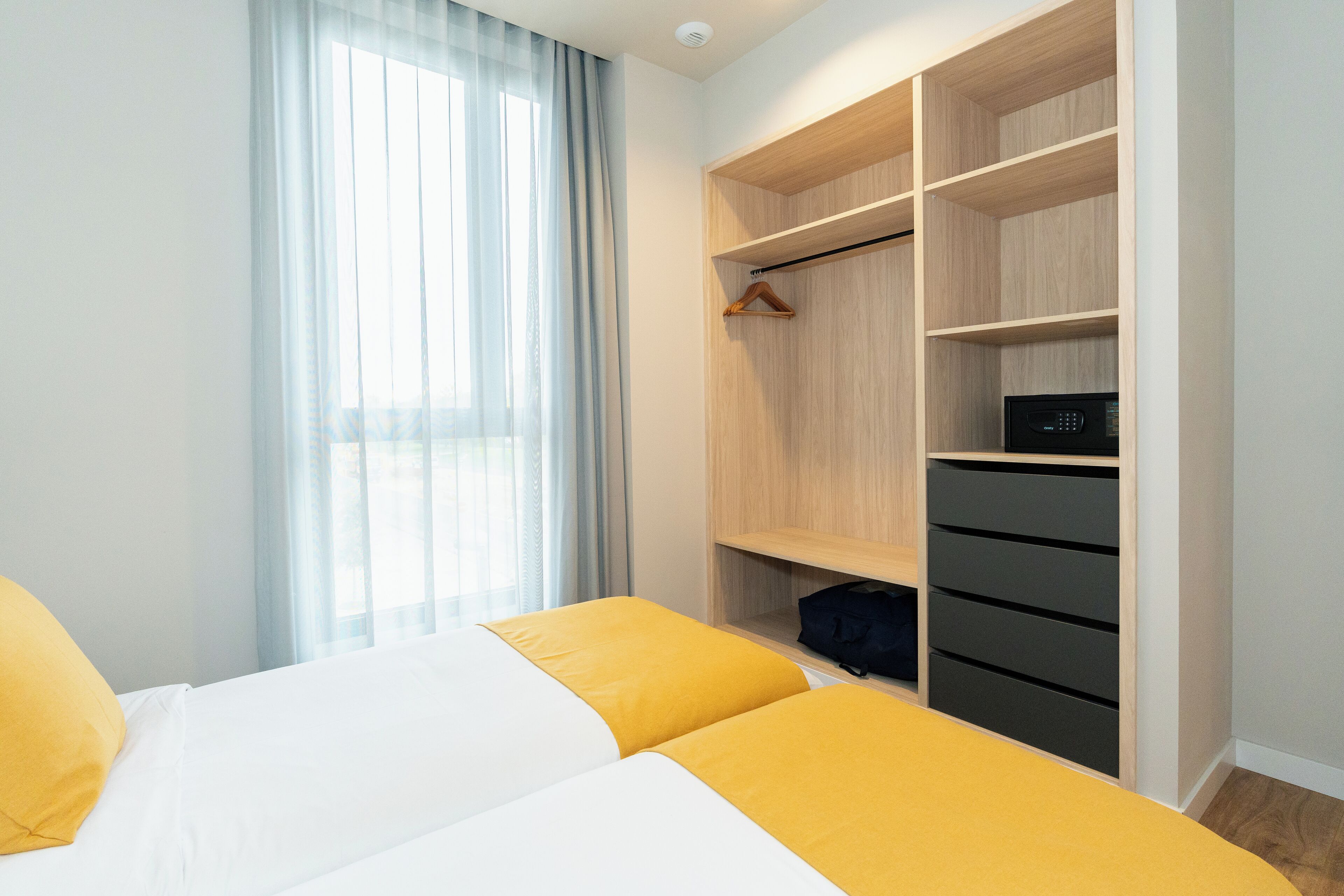 A hotel room with a bed, a wardrobe with multiple shelves, and a window with curtains.