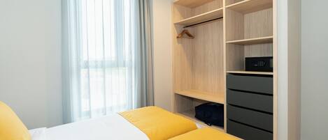 A hotel room with a bed, a wardrobe with multiple shelves, and a window with curtains.