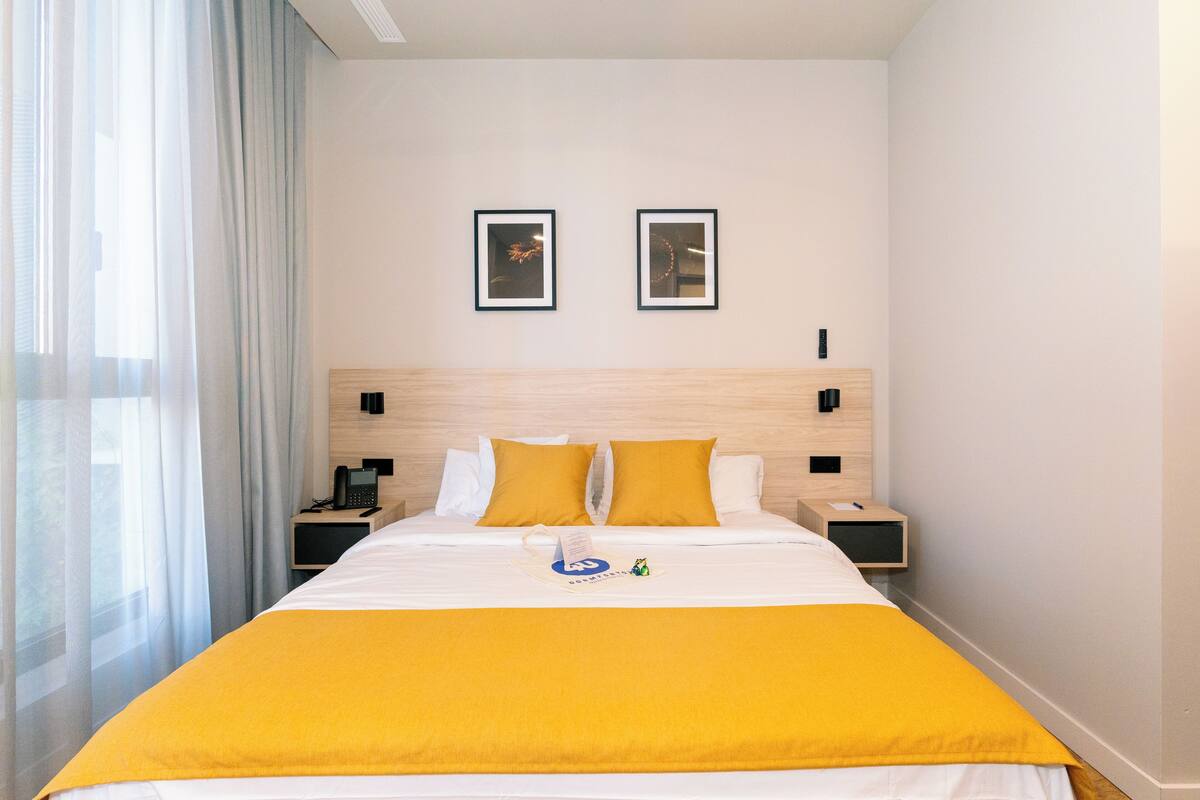 A hotel room with a bed, two bedside tables, a nightstand, a telephone, and two framed pictures on the wall.