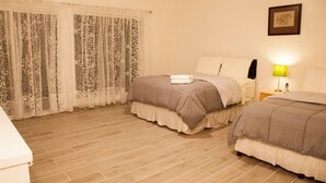 Ein Hotelzimmer mit zwei Betten, Holzboden, einem Fenster mit gemusterten Vorhängen, einer Nachttischlampe und einem gerahmten Bild an der Wand.
