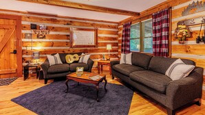 Une pièce chaleureuse, aménagée dans le style d’un chalet en rondins, avec deux canapés, une table basse et un plafond en bois.