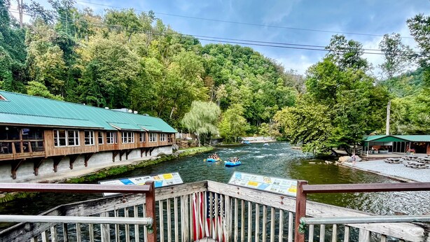 Une terrasse en bois offrant une vue sur une rivière, des radeaux et un bâtiment doté d’un toit végétalisé.