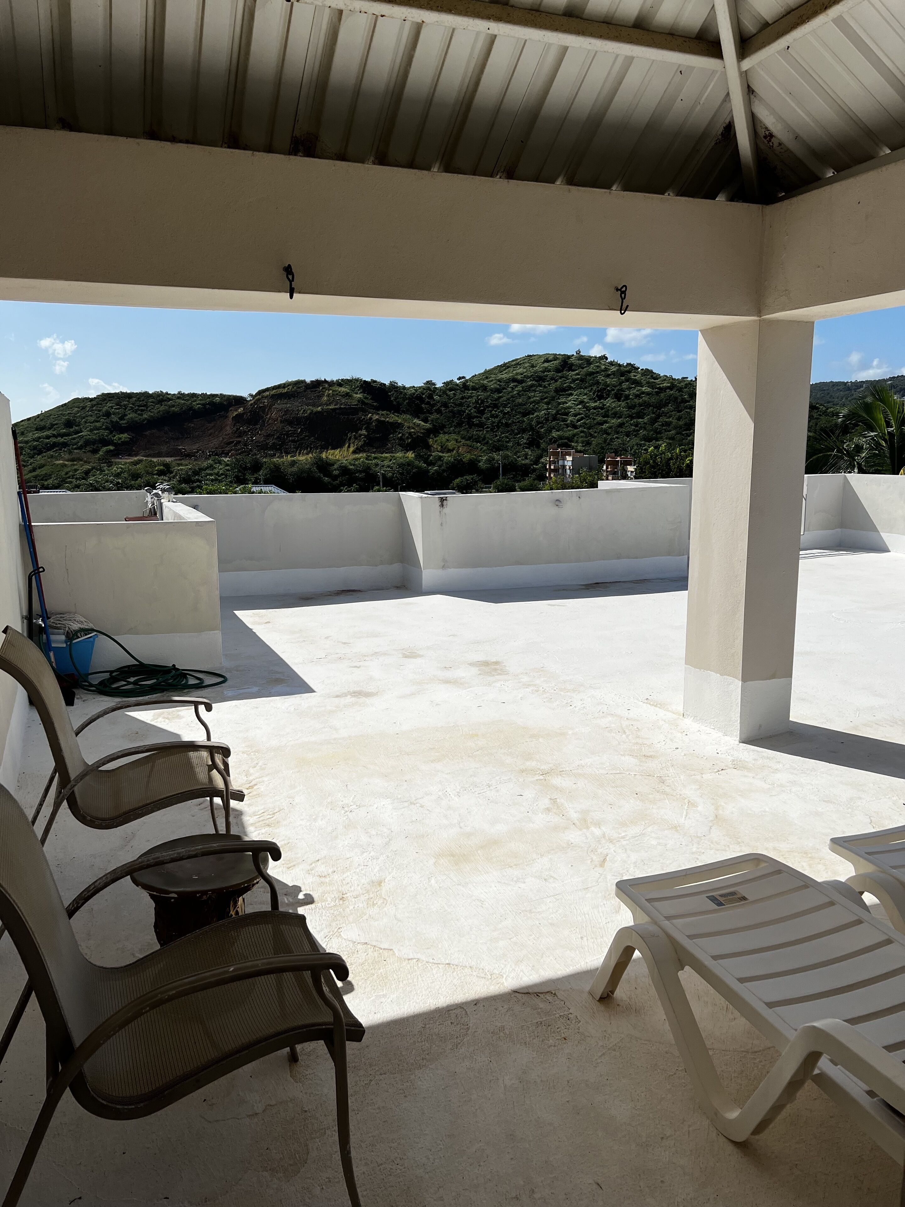 Un espace extérieur abrité, aménagé avec des chaises et une table, offrant une vue sur un paysage vallonné.