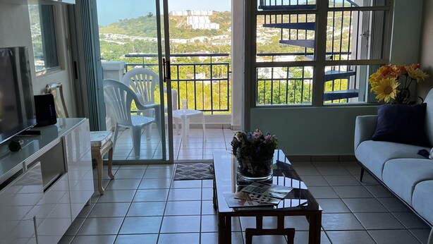A modern living room with a balcony, a ceiling fan, and a view of the cityscape. - Family friendly place for those looking for adventure, beach, and great food! (Ceiba)