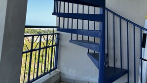 A blue spiral staircase with a metal railing, leading to an outdoor balcony with a view of greenery and buildings. - Family friendly place for those looking for adventure, beach, and great food! (Ceiba)