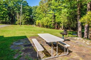 Une table de pique-nique avec des bancs, située dans un espace herbeux entouré d’arbres.