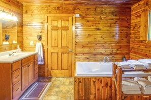 Une salle de bain rustique, avec des murs et une porte en bois, un lavabo, une baignoire et un miroir.