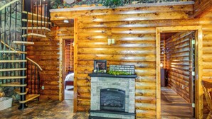 Interior de una cabaña de troncos con chimenea de piedra, una escalera en espiral y techo de madera.