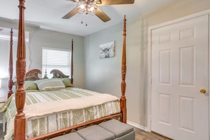 A four-poster bed with a wooden headboard, a ceiling fan, and a white door with a gold doorknob.