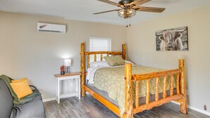 A bedroom with a wooden bed, a ceiling fan, an air conditioning unit, a bedside table with a lamp, and a window with blinds. - Oklahoma Home Near Lake w/ Patio, Grill & Chiminea (Fort Cobb)