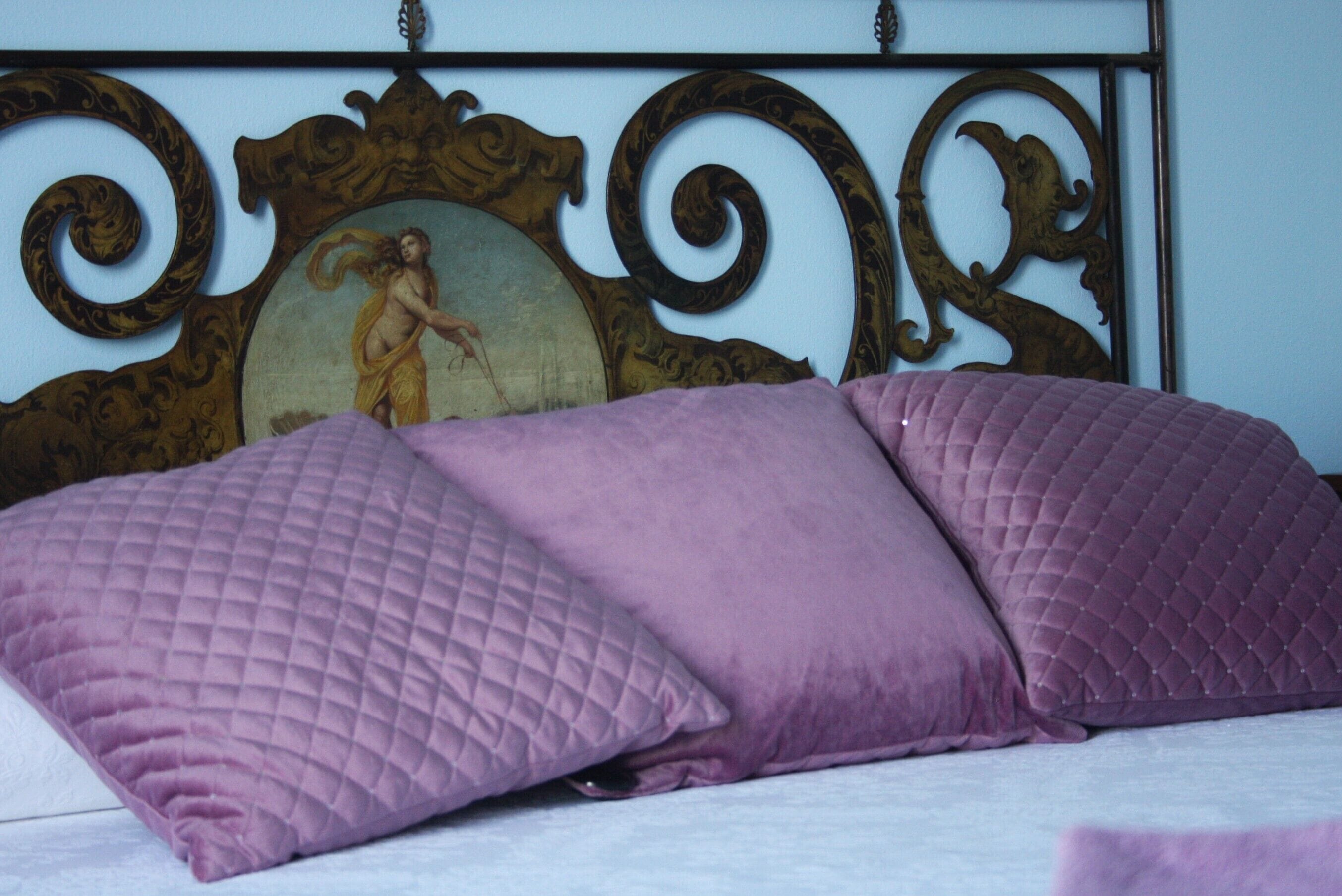 A bed with a headboard featuring an ornate design and a framed artwork.