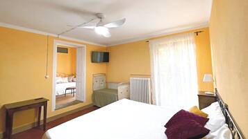 Ein Schlafzimmer mit Bett, Deckenventilator, Heizkörper, Fernseher und einem Fenster mit Vorhängen.