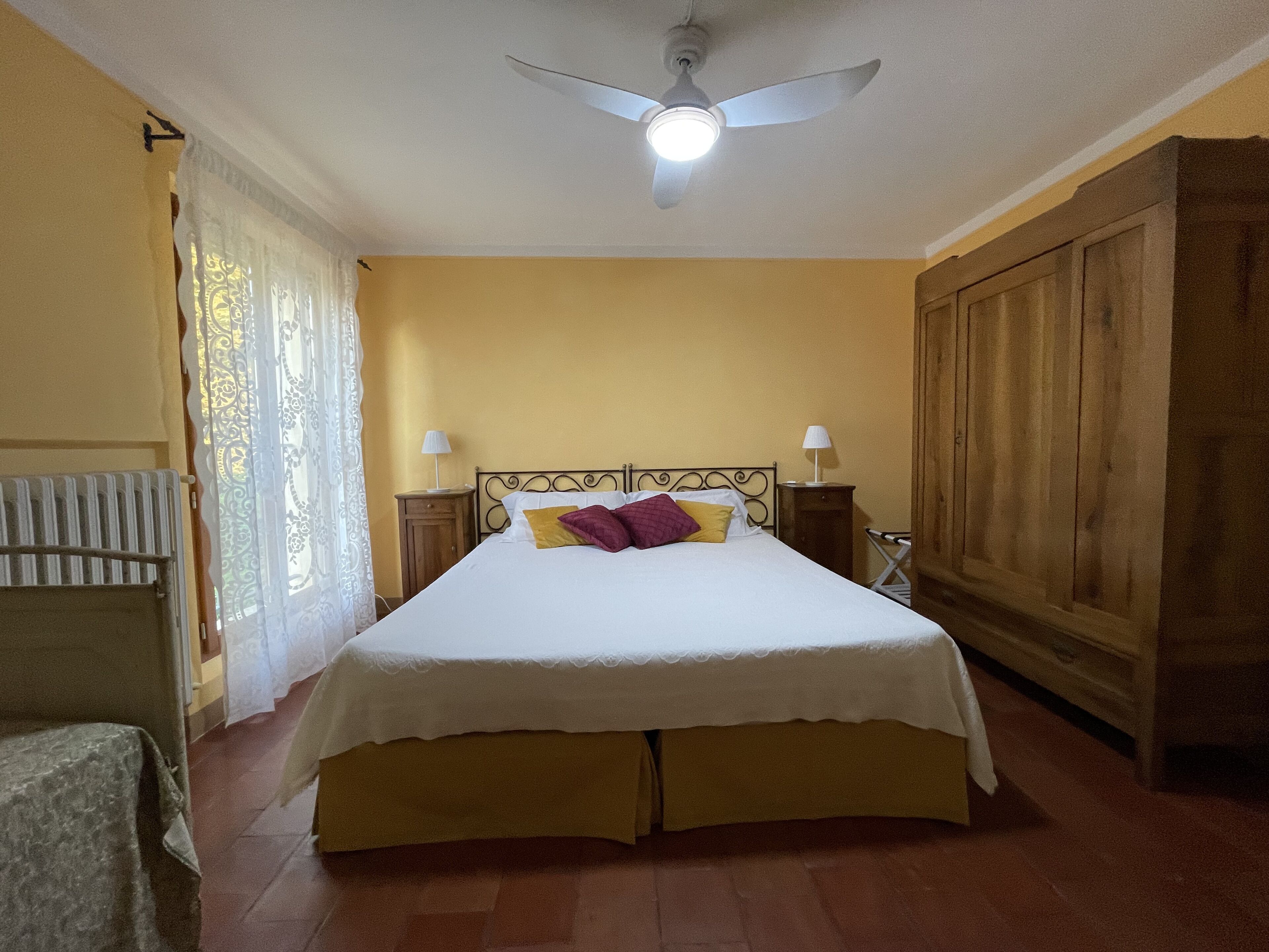 A bedroom with a bed, two bedside tables, a ceiling fan, and a radiator.