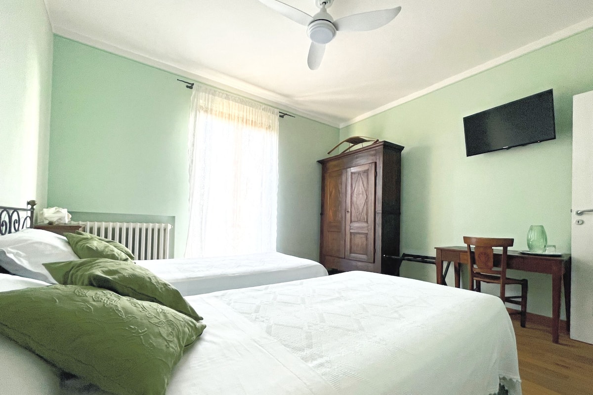 Een slaapkamer met twee bedden, een plafondventilator, een houten garderobe, een bureau met stoel en een flatscreen-televisie aan de muur.