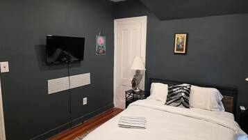 A bedroom with a bed, a television mounted on the wall, a door, and a small table with a lamp.