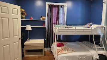 Une chambre à coucher avec un lit superposé, une table de chevet, une lampe, une étagère avec des objets décoratifs et une porte.