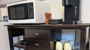 Een keukenhoek met een magnetron, koffiezetapparaat en divers keukengerei op een houten kast.