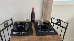 Een eettafel met zwarte placematen, twee wijnglazen en een fles rode wijn.