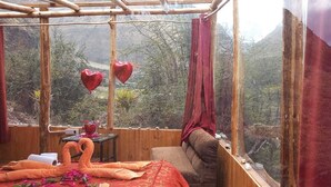 A cozy room with a wooden bed, a small table with a vase, and a view of a mountainous landscape. - Refugios Salkantay (Mollepata)