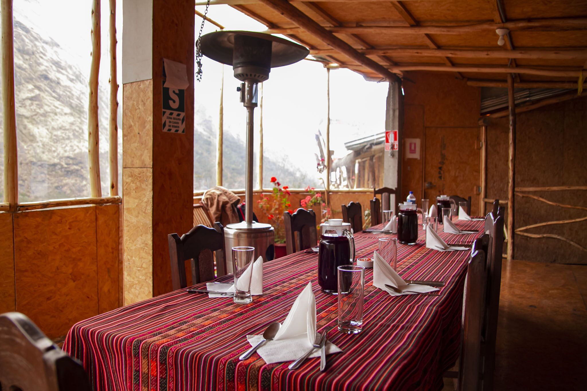 A dining area with a long table set for a meal, a hanging light fixture, and a view of the outdoors.