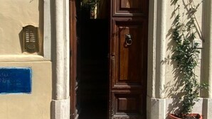 Una porta in legno con maniglia in metallo, una pianta in vaso alla destra e un ingresso con lastricato in pietra.