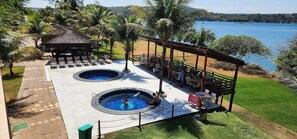 A pool area with two hot tubs, lounge chairs, and a covered seating area overlooking a lake. - Aldeia do Lago (Caldas Novas)