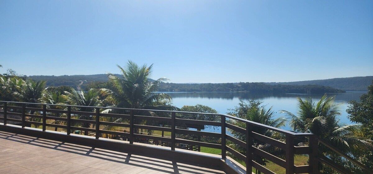 Un balcon doté d’une balustrade en bois, donnant sur un lac paisible, et entouré de palmiers et de verdure.