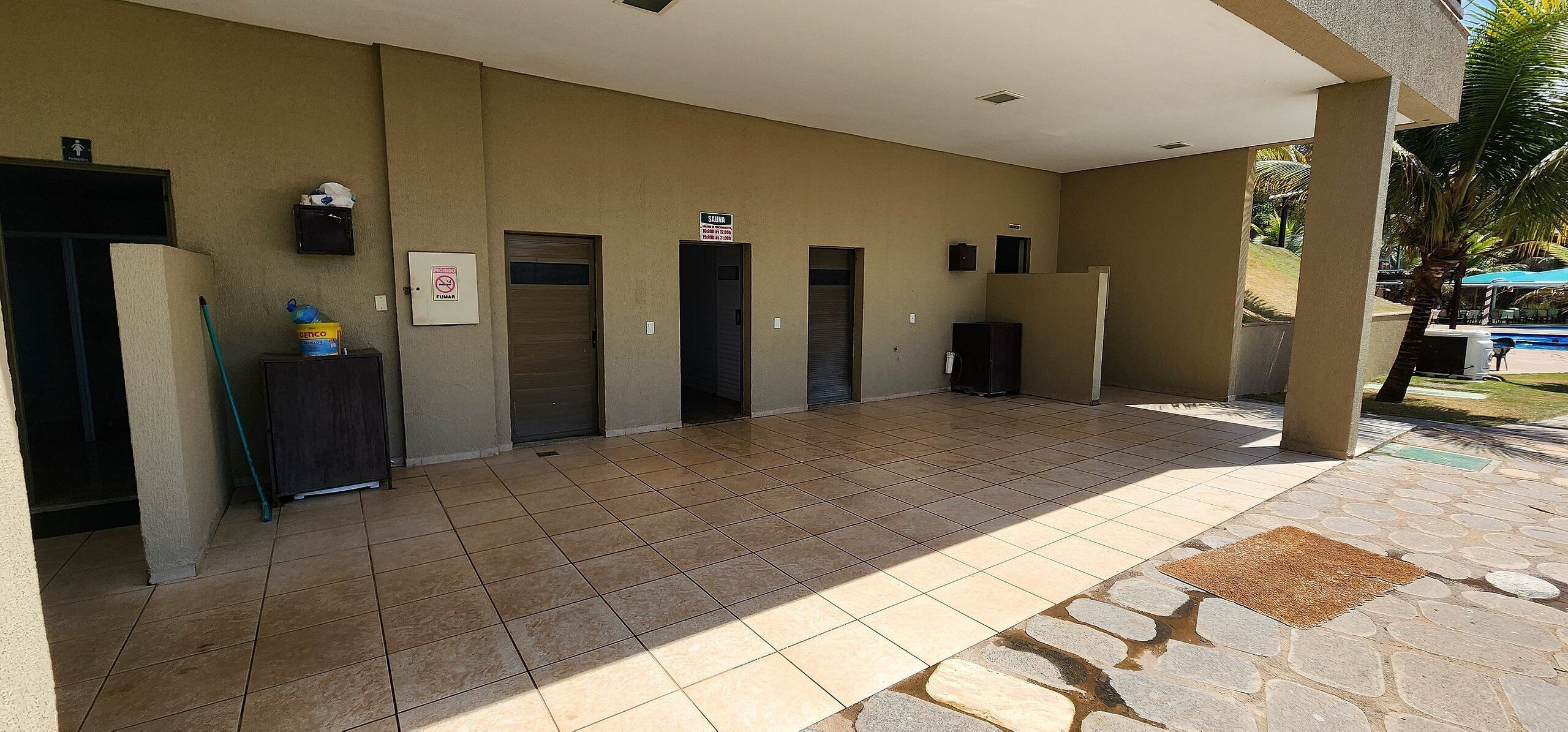 A covered outdoor area with tiled flooring, multiple doors, a water dispenser, and a sign indicating a smoking area.