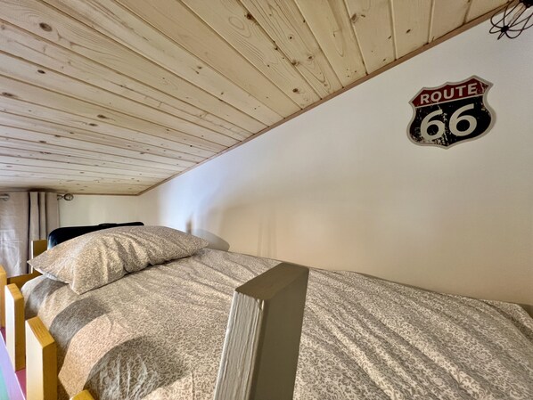 Una cama litera con una colcha estampada, techo de madera y un cartel en la pared que indica la Ruta 66.