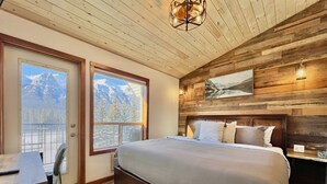 A bedroom with a large bed, wooden walls, a desk, and a chair.