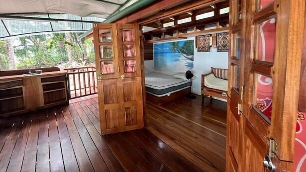 Una terraza de madera con una cama, un banco y un ventilador.