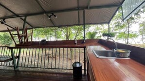 Un espacio de estar al aire libre techado, con un banco de madera, barandilla de metal y un lavabo.