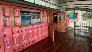 Una terraza cubierta de madera con un muro rosa con paneles decorativos y una puerta que da a un espacio interior.