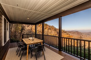 A covered outdoor patio with a wooden table and chairs, overlooking a scenic mountainous landscape.