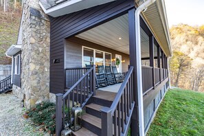 A stone and wood building with a covered porch, steps, and a number sign.